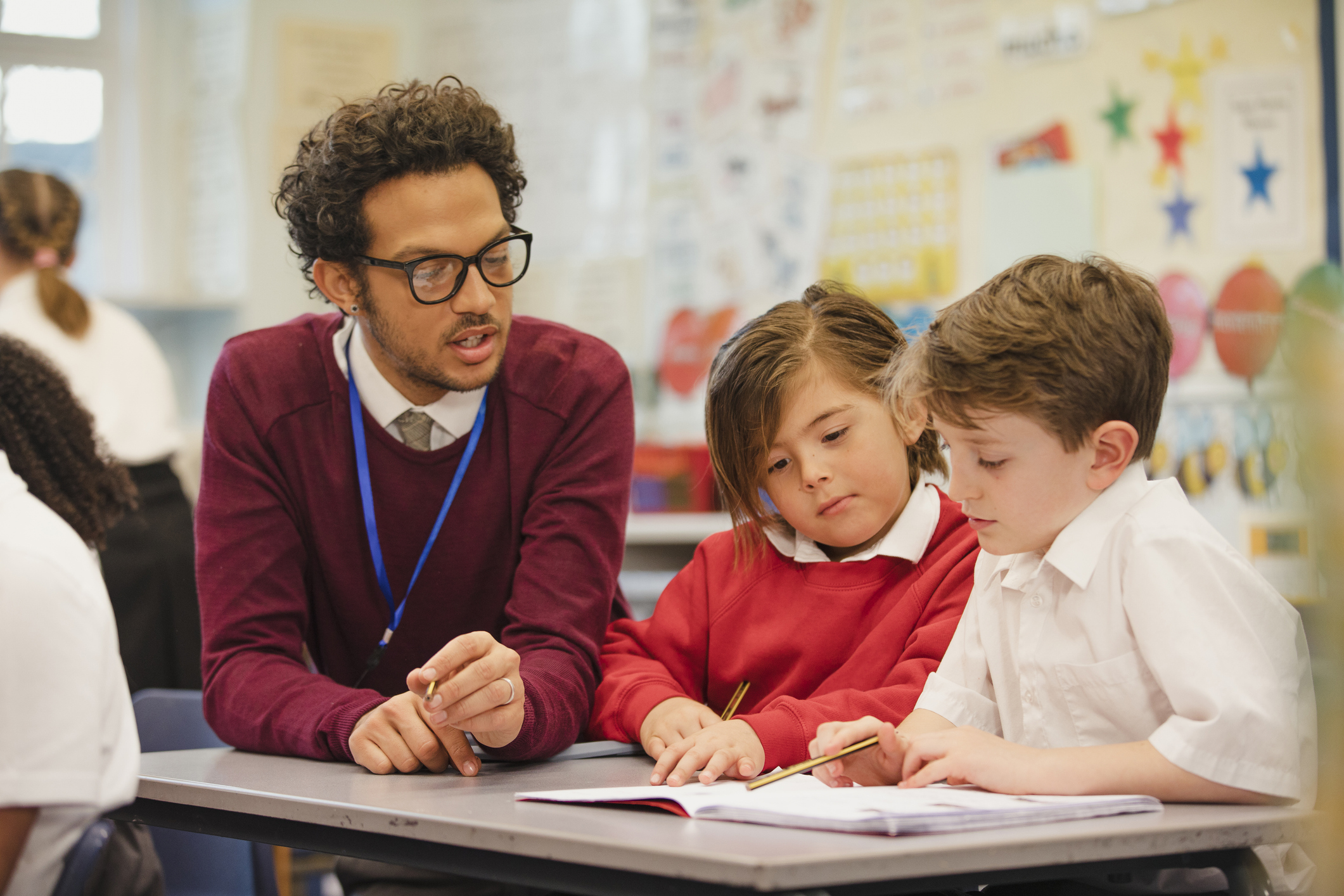 Two schoolboys work through a textbook with their teacher in elementary class. This is a school in Hexham, Northumberland in north eastern England.
